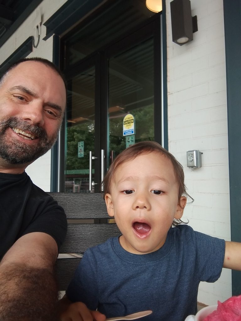 Smiling man and child eating ice cream outside.